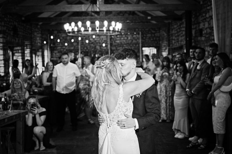 B&W image of a Bride & groom kissing whilst doing their first dance.