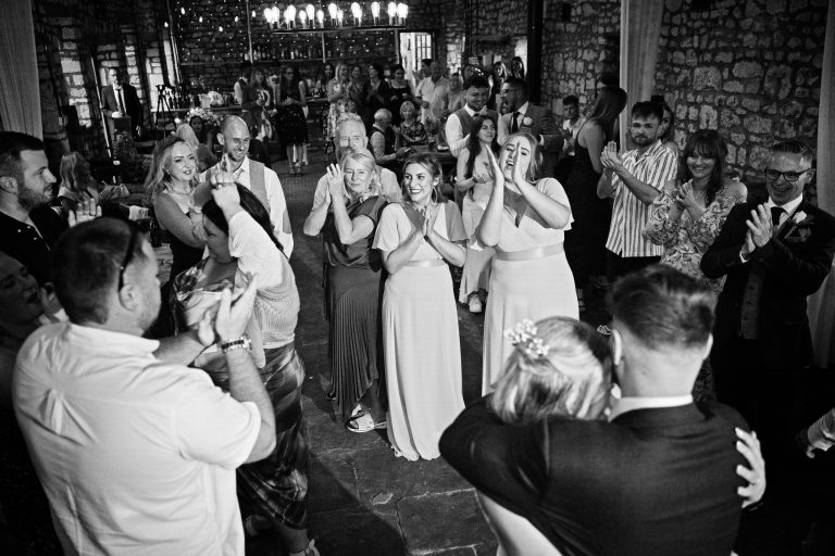 B & W image of wedding guests clapping at their bride & groom in celebration of their first dance.