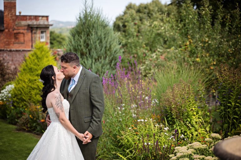 bride and groom kiss romantically with a gorgeous Georgian house and gardens are behind them.