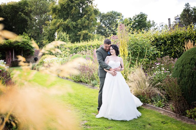Bride and groom surrounded by gorgeous plants hug and smile together