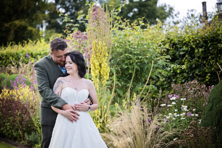bride and groom embracing smiling with gorgeous summer plants behind them.