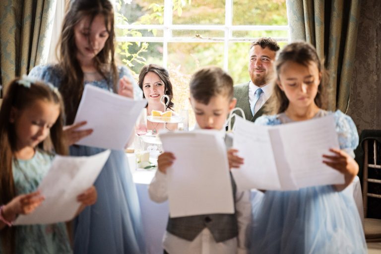 bride and groom look onward to their children who are reading a poem about the wedding.