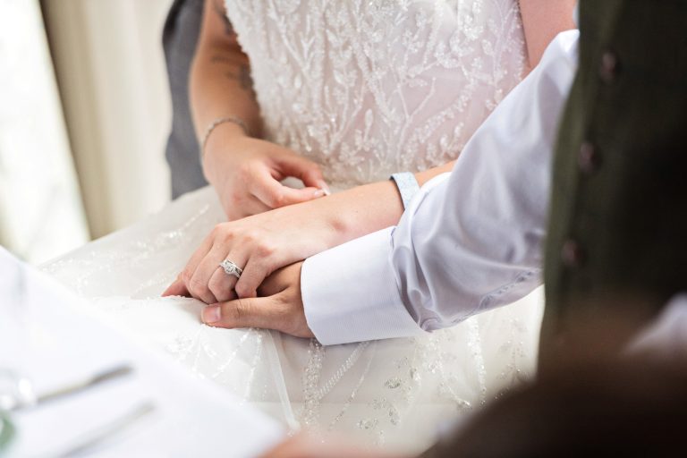 a bride and groom holding hands at a dinner table with the new wedding ring showing.