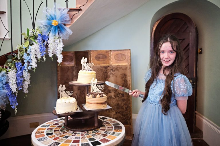 A flower girl cheekily about to cut her mum and dads wedding cake.
