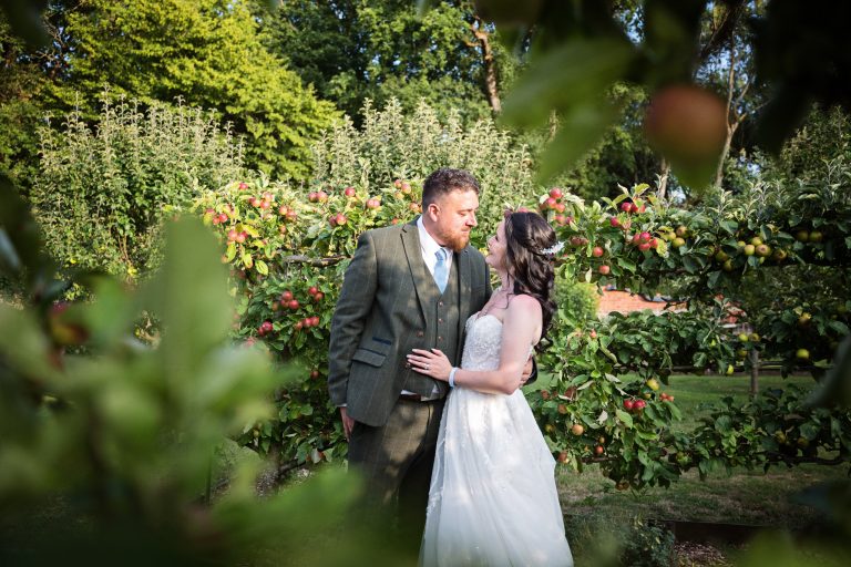 bride and groom holding each other smiling and surrounded by apple trees and fruit.